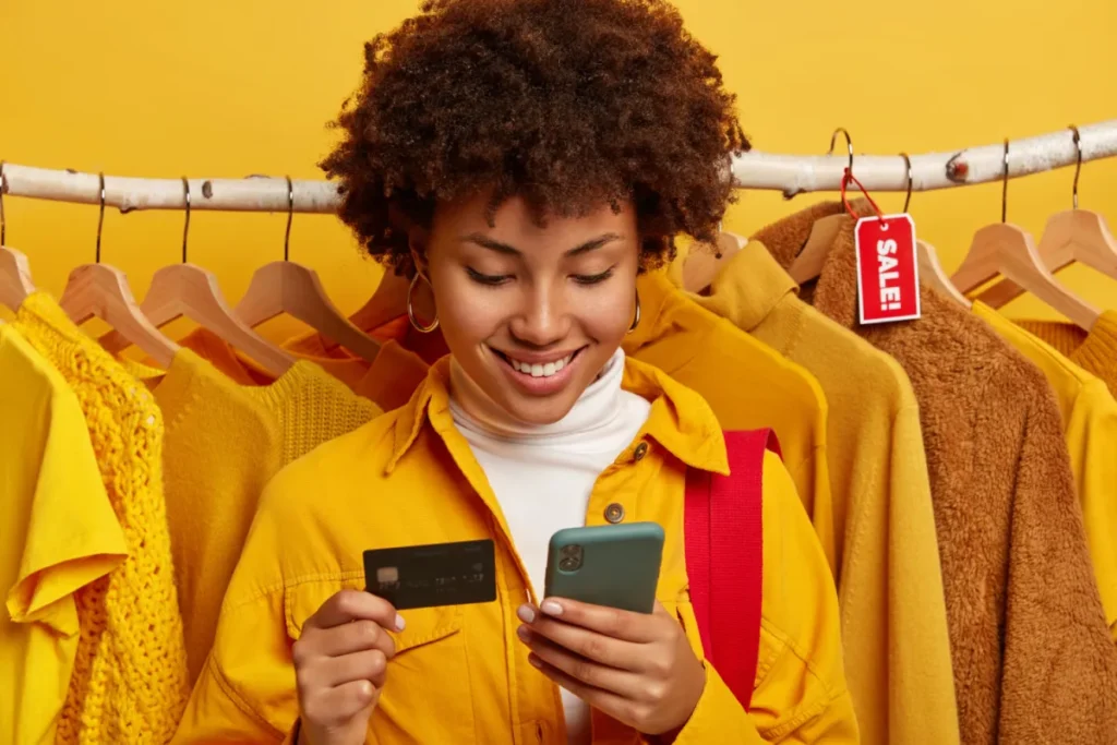 woman with yellow jackets on phone opening email with credit card in hand 