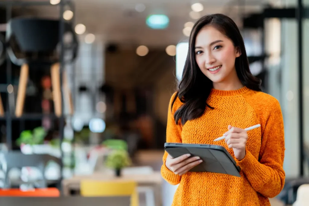 Young woman standing in front of a store with an iPad and a pencil looking at the camera smiling, she is measuring the effectiveness of her campaign with the data driven approach